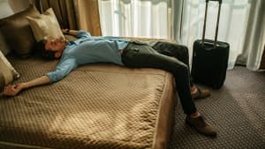 Ein Mann liegt erschöpft von der Anreise auf einem Hotelbett