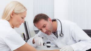 Arzt führt in seiner Praxis eine Dermatoskopie-Prävention bei einer Patientin durch.