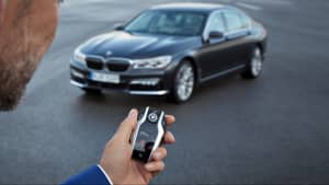 Mann hält einen Autoschlüssel von BMW in der Hand. Im Hintergrund steht ein 7er BMW