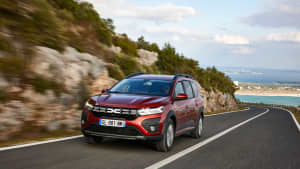 Ein terracotto-roter Dacia Hybrid währdend der Fahrt am Meer