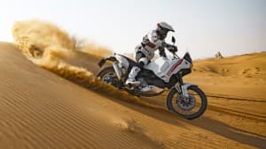 Seitenansicht einer durch die Wüste fahrenden Ducati Desert X