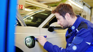 TÜV Süd Mitarbeiter überprüft mit einer Taschenlampe die Ladeeinheit eines Elektroautos