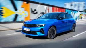 Ein blauer Opel Astra Electric fährt an einem Grafitti vorbei