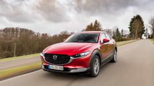 Ein roter Mazda CX-30 während der Fahrt, von vorne an einem wolkigen Tag