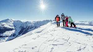 Eine Familie mit Skiern im Schnee im Hintergrund sieht man die Kitzbühler Alpen