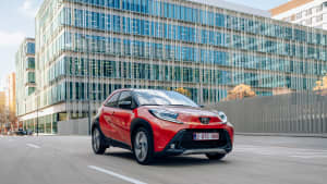 Ein neuer, roter Toyota Aygo X waehrend der Fahrt durch die Stadt von vorne