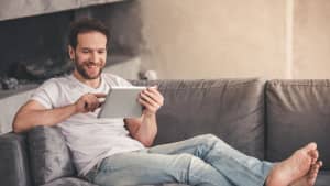 Ein Mann liegt auf dem Sofa mit einem Tablet in der Hand