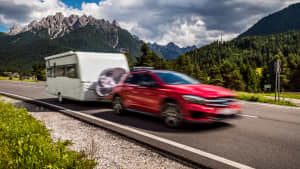 Ein rotes Auto zieht einen Wohnwagen vor einer Bergkulisse