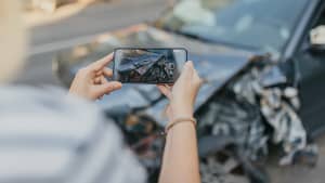 Nahaufnahme der Hände einer Frau, die ein Foto eines Unfallautos mit em Handy macht