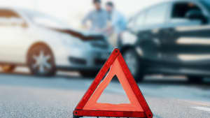 Ein Warndreieck auf einer Strasse, im Hintergrund ein Unfall