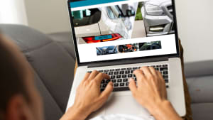 Ein Mann sitzt an einem Laptop und schaut auf ein Auto auf dem Bildschirm.