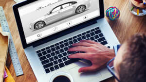 Ein Mann sitzt an einem Laptop mit einer Tasse Kaffee in der Hand und schaut auf ein Auto auf dem Bildschirm.