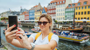 Eine Frau macht ein Selfie vor einer Häuserzeile mit bunten Häusern.