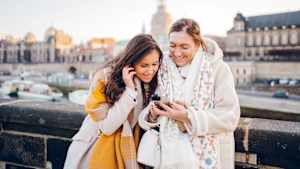 Zwei frauen schauen auf ein Mobiltelefon und lachen gemeinsam