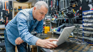 Mechaniker lehnt über dem Laptop in einer Autowerkstatt