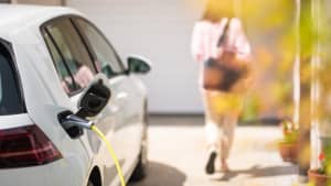 Eine Frau geht in ihr Haus während das Elektroauto aufgeladen wird