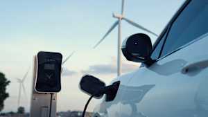 Ein Elektroauto lädt an einer Ladesäule. Im Hintergrund sind Windräder zu sehen.