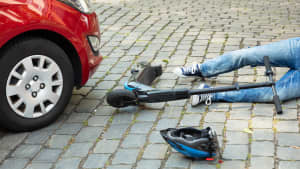 Ein E-Scooter-Fahrer liegt vor einem Auto auf der Strasse