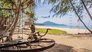 Ein Strand in Thailand mit einem Flugzeug im Landeanflug zu sehen  im Hintergrund