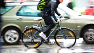 Ein Fahrradfahrer fährt auf einer nassen Straße in der Dämmerung neben einem Auto