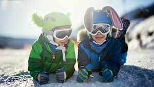 Zwei Kinder in Schneeausrüstung liegen auf einem schneebedeckten Boden