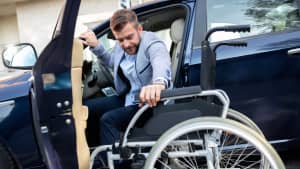 Ein Mann mit Gehbehinderung steigt von seinem Auto in seinen Rollstuhl