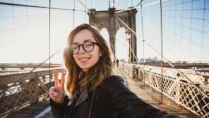 Eine junge Frau steht lachend auf der Brooklyn Bridge