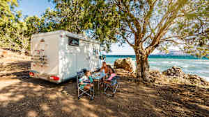 Eine Familie steht mit ihrem Wohnmobil in Griechenland mit Ausblick aufs Meer