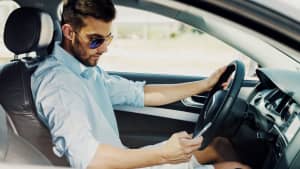 Mann schaut während der Autofahrt auf sein Handy
