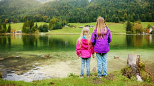 Zwei junge Mädchen die im Herbst vor einem Bergsee stehen und auf das Wasser sehen