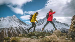 Junges Paar hüpft über die Steine dahinter Berggipfel