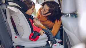 Eine Mutter schnallt ihr Kind im Kindersitz auf der Rückbank eines Autos an