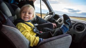 Ein Kind, das auf dem Vordersitz im Kindersitz auf einem großen Wohnmobil sitzt und glücklich lächelt