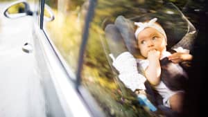 ein Baby sitzt in einem Kindersitz und nuckelt an den Fingern