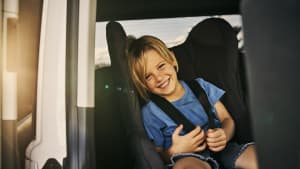 Kind sitzt lachend und angeschnallt im Kindersitz