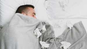 Ein Mann liegt mit vielen benutzen Taschentüchern krank im Bett