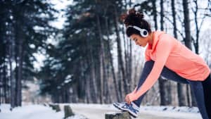 Eine Frau bindet sich die Turnschuhe während einer Jogging-Runde im Wald im Winter