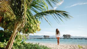 Frau steht auf einem tropischen Strand mit Kokospalmen und türkisfarbenem Meer und genießt ihren Urlaub auf den Malediven