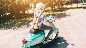 Eine Frau auf einer Vespa fährt auf einer Landstraße