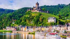 Eine Stadt an einem Fluss, mit Schiffen und über der Stadt liegt eine Burg auf einem Berg