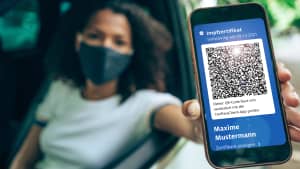 Eine junge Frau, die in ihrem Auto sitzt und ein Smartphone mit gültigem digitalem Impfausweis für COVID-19 zeigt.