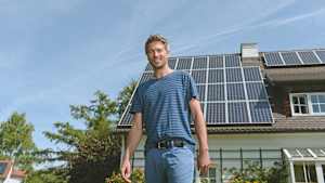 Ein Mann steht vor seinem Haus mit PV Anlage auf dem Dach