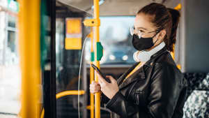 Junge Frau steht mit ihrem Handy in einem Bus