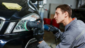 Junger Mechaniker poliert einen Autoscheinwerfer