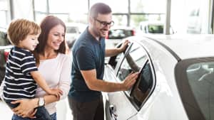 junge Familie begutachtet ein neues Auto beim Händler