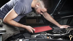Mechaniker beugt sich über einen Motor und hat einen neuen Luftfilter in der Hand.