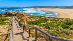 Frau blickt auf einem Steg auf das Meer und den Praia da Bordeira in Portugal