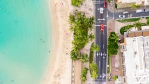 Drohnen Bild von einer Küstenstrasse auf Hawaii, mit Meer, Palmen, Straße und Häusern.