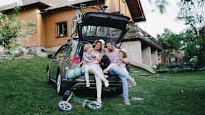 Eine Familie sitzt im Kofferraum ihres Autos vor dem Ferienhaus
