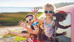 Familie schaut aus dem Auto und winkt